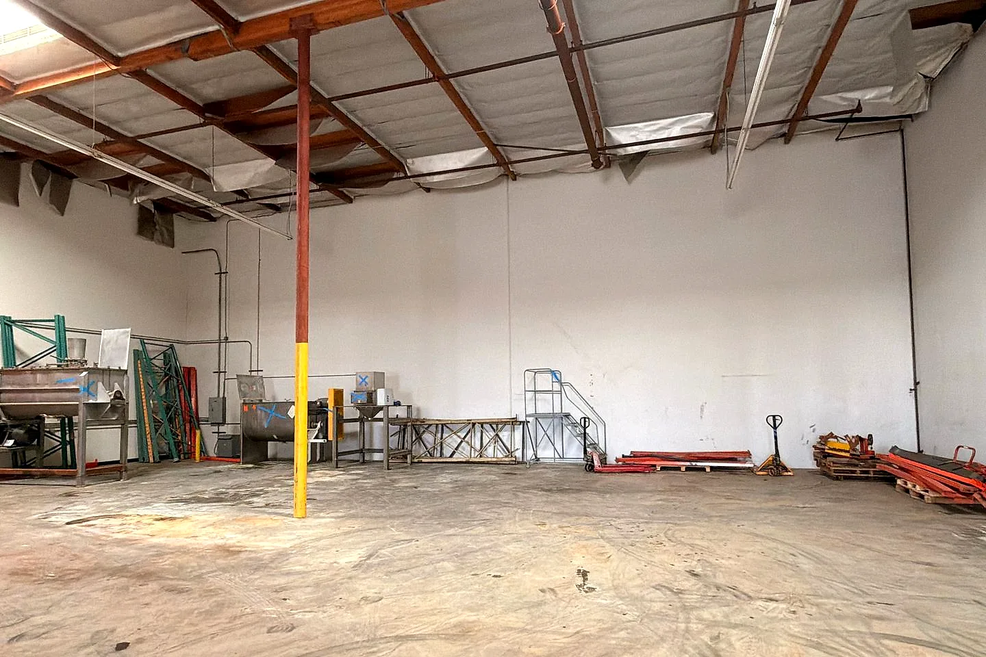 Large empty warehouse with a clear concrete floor and a yellow support column after cleanout
