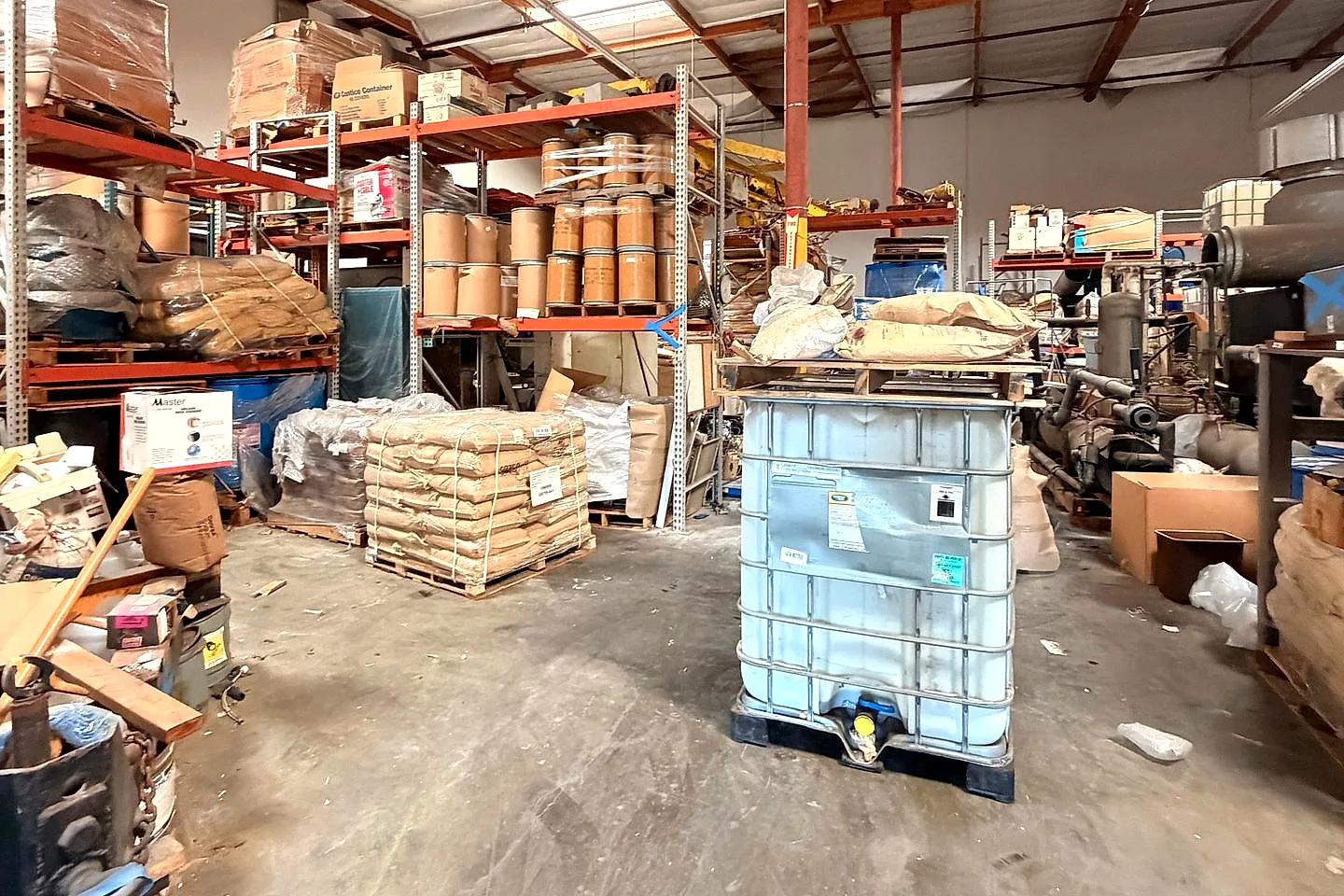 Warehouse aisle packed with racking, pallets of bagged material, and an intermediate bulk container before cleanout